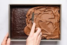 a person is spreading chocolate frosting on a cake in a pan with a knife