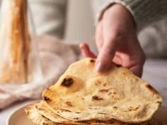 a stack of flatbreads on a plate with a hand reaching for the top