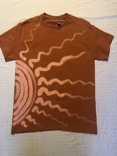 a brown t - shirt with white swirls on it sitting on top of a bed