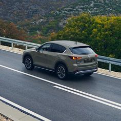 a gray car driving down the road next to a forest and mountain range in the background