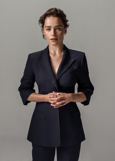 a woman standing with her hands folded in front of her chest and wearing a blue suit