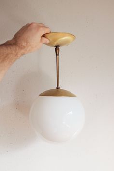 a hand is holding a light fixture on the wall with a white ball hanging from it