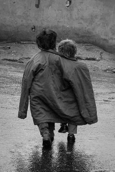 two people walking in the rain with an umbrella over their heads and one person holding on to his back