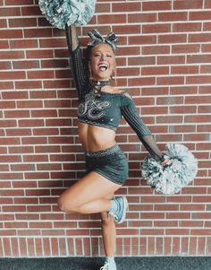 a cheerleader is posing in front of a brick wall with her pom poms