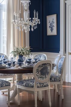 an elegant dining room with blue walls and white chairs, chandelier and table