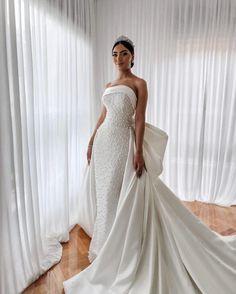 a woman in a white wedding dress standing next to a window with curtains behind her