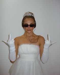 a woman wearing white gloves and a tiara holding two fingers up in the air