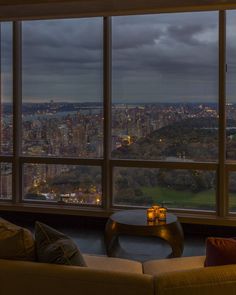 a living room filled with furniture and large windows overlooking the city at night, as seen from an upper level window