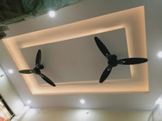 two black ceiling fans mounted to the ceiling in a room with white walls and lights