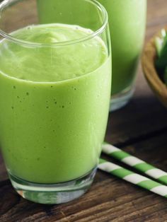 two glasses filled with green smoothie sitting on top of a wooden table