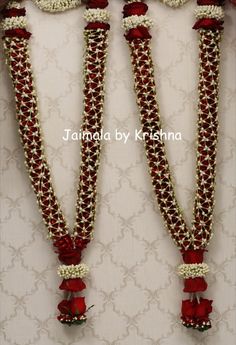 three red and white necklaces with flowers on them, hanging from the side of a wall