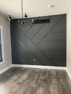 an empty room with wood flooring and black painted wall behind the chandelier