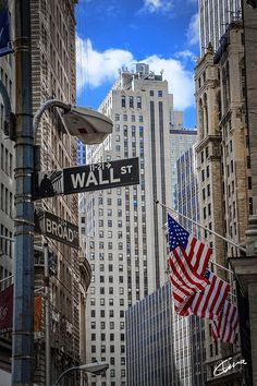 an american flag hanging from a street sign in the middle of a city with tall buildings