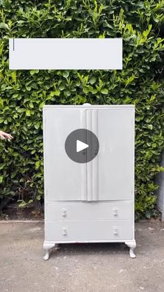 a white cabinet sitting in front of a green hedge