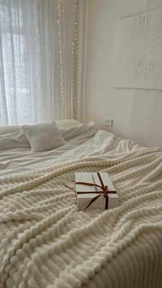 a gift wrapped in brown ribbon on top of a white bed covered in blankets and pillows