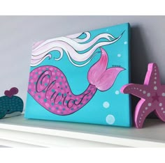 a painting of a mermaid and starfish on a shelf next to a wooden sign