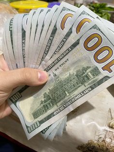 a person holding money in their hand over a pile of other bills on a table