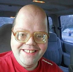 a man wearing glasses sitting in the back seat of a car smiling at the camera