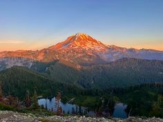 the sun is setting over a mountain range with a lake and trees in front of it