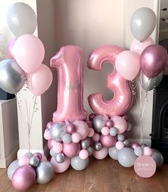 the number thirteen is surrounded by balloons in pink, silver and grey colors on a wooden floor