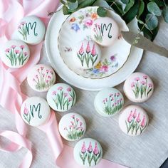 some pink flowers are sitting on a plate next to other buttons and ribbons with the letter m painted on them