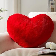 a red heart shaped pillow sitting on top of a couch next to a white rose