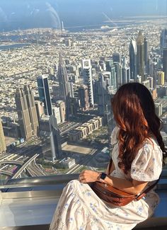 a woman sitting on top of a tall building looking out over a cityscape