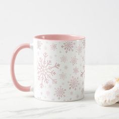 a pink and white snowflake mug next to a donut