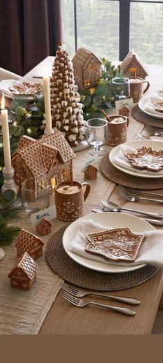 a table set for christmas dinner with gingerbread houses on the plates and silverware