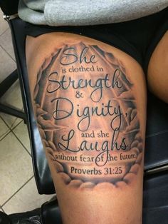 a woman's leg with a bible verse tattoo on her thigh and the words she is clothed in strength and eighty and she laughs without fear of the future prove