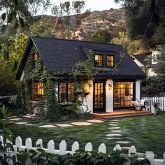 a small house with a black roof and white picket fence in front of the house