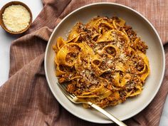 a white bowl filled with pasta and meat on top of a brown cloth next to a spoon