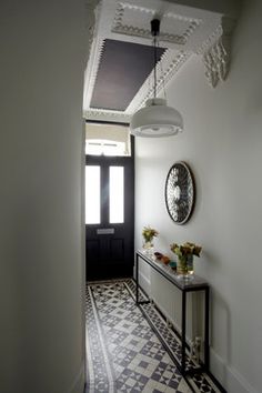 a hallway with a black and white checkerboard floor, an ornate ceiling light and a mirror on the wall