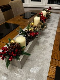 a long wooden table with candles and christmas decorations on the top, along with pine cones