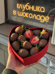 a person holding a heart shaped box filled with chocolate covered strawberries in front of a store window