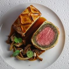 a white plate topped with a piece of meat covered in sauce next to some vegetables