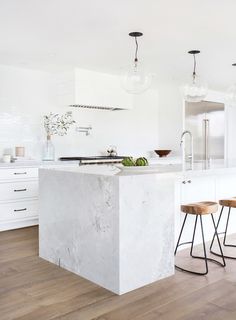 a white kitchen with marble counter tops and stools next to an island in the middle