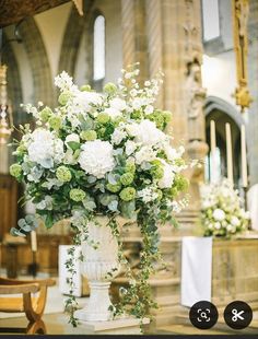 a vase filled with white and green flowers sitting on top of a table in front of a church