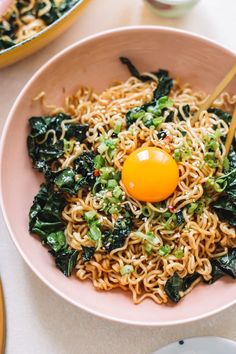 a pink bowl filled with noodles and an egg on top of it next to chopsticks