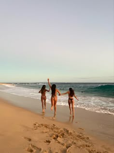 three girls running on the beach with their arms in the air and footprints in the sand