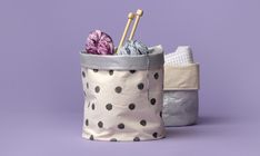 a white and black polka dot fabric basket with yarn in it on a purple background