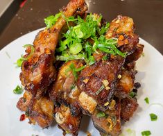 a white plate topped with chicken wings covered in green onions and garnished with scallions