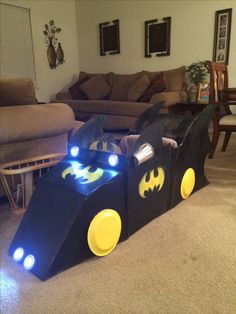 a child's batman car made out of cardboard sitting on the floor in front of a couch