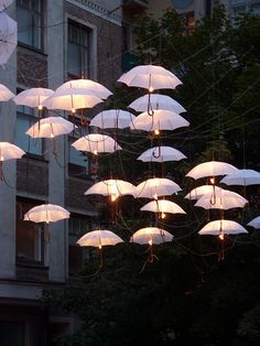 many white umbrellas are hanging in front of a tall building at night with lights on them