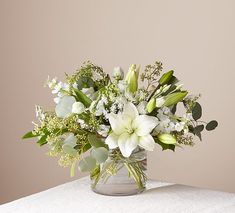 a vase filled with white flowers and greenery on top of a table next to a wall