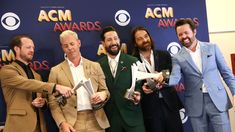 five men in suits posing for a photo at the acm awards with their trophies