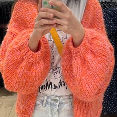 a woman taking a selfie with her cell phone in an orange cardigan sweater