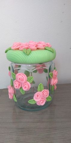 there is a glass jar with pink flowers on the lid and green leaves around it