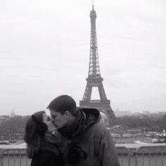 a man and woman kissing in front of the eiffel tower on a cloudy day