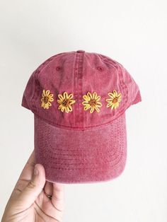 a person holding up a red hat with yellow flowers on the front and side of it